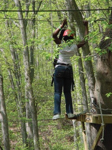 Photo of a high ropes course participant clipped into an upper safety cable and standing on a lower cable
