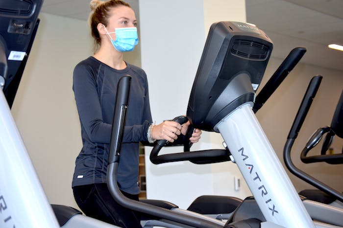 A woman in a facemask jogs on a Matrix treadmill
