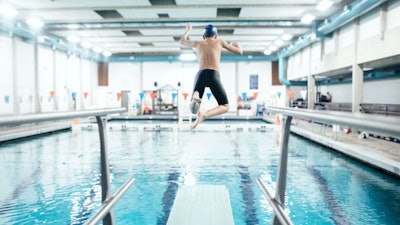 Boy jumping off a diving board into an indoor pool