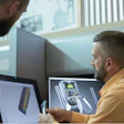 Two people examine a prototype near a computer
