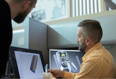 Two people examine a prototype near a computer