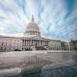 U.S. Capitol building under dramatic clouded sky with reflective marble plaza