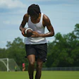 Athlete in white tank top catching football on green soccer field