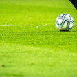 Soccer ball on bright green field with player's cleat ready to kick