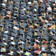 Crowded graduation ceremony with sea of black graduation caps and decorated caps