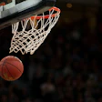 Basketball hovering beneath orange hoop with white net in dramatic lighting