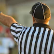 Sports referee signaling with raised arm, wearing striped black and white shirt