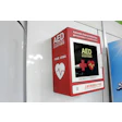 Emergency AED defibrillator mounted on white wall, red device with heart health icon