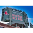 Fenway Park entrance sign with Boston Red Sox logo and red sock emblems on green background against blue sky