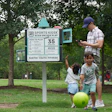 Children playing near Sports Kiosk in green park with large green ball