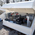 White industrial pump system enclosed in protective housing on gravel ground
