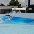 Surfer riding artificial wave at indoor surf park with blue water