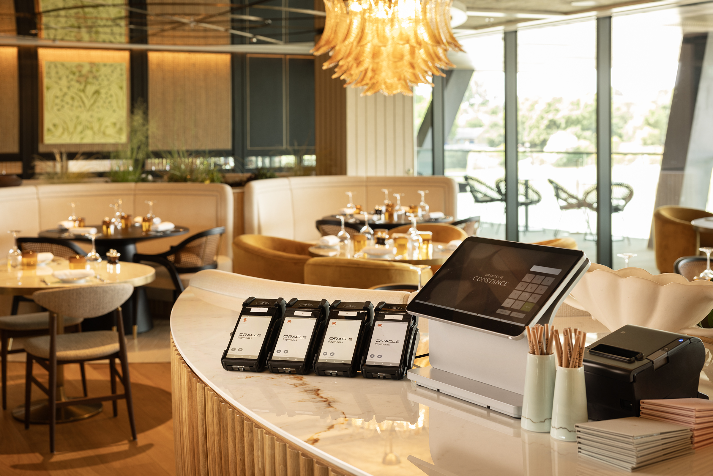 Modern restaurant interior with curved counter, point-of-sale system, and elegant gold chandelier