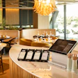 Modern restaurant interior with curved counter, point-of-sale system, and elegant gold chandelier