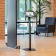Digital check-in kiosk with screen display near armchair in modern brick-walled lobby
