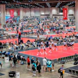 Crowded indoor volleyball tournament with multiple red and blue courts and spectators
