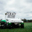 White and green autonomous robotic lawn mower on grassy field with trees