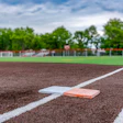 Baseball field with white foul line and base, green grass and brown dirt infield