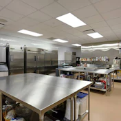 Commercial kitchen with stainless steel appliances, prep tables, and industrial refrigerators