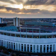 Historic white and blue stadium with arched design at sunset, aerial cityscape view