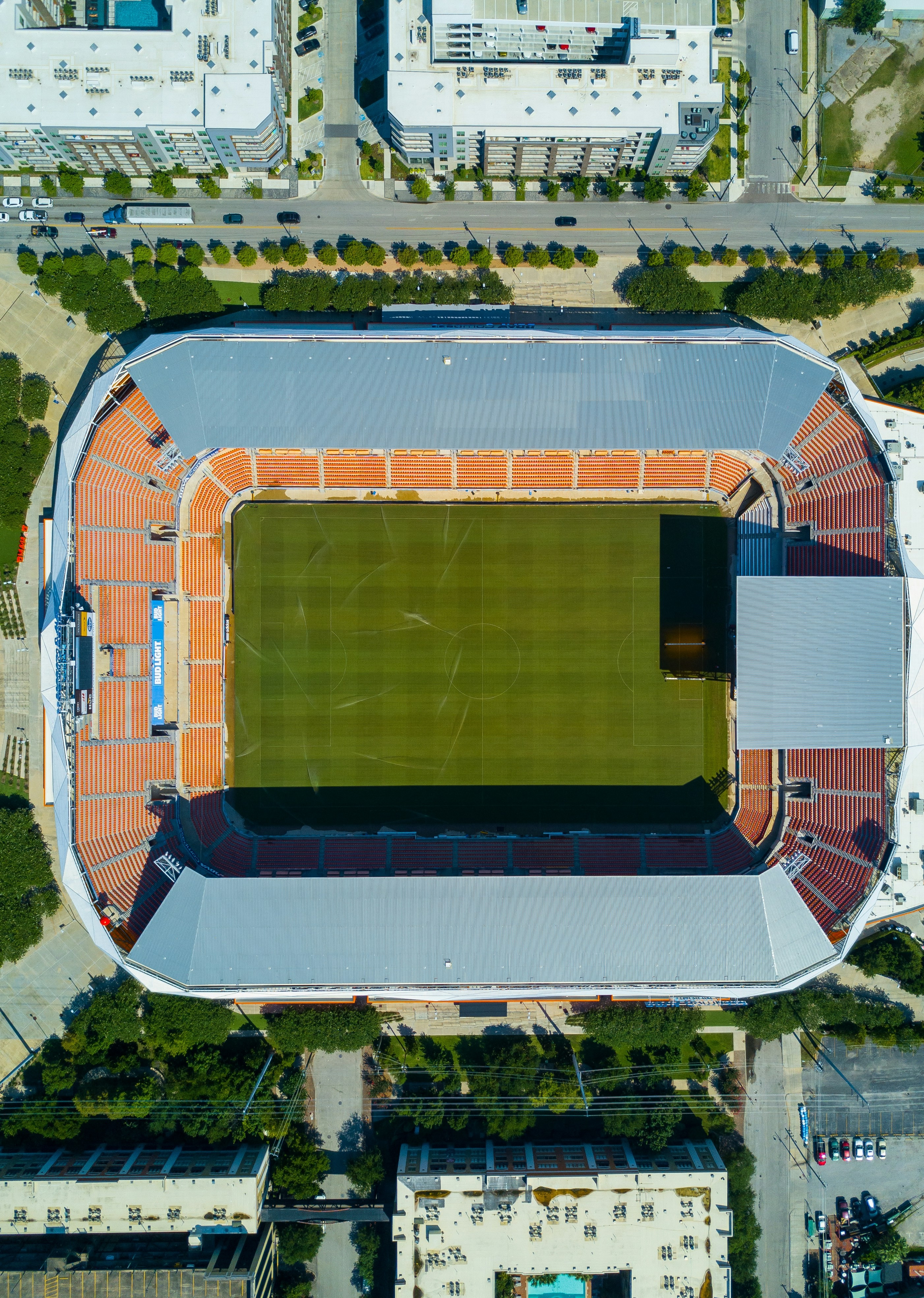 Aerial view of soccer stadium with orange seats and green playing field in urban setting