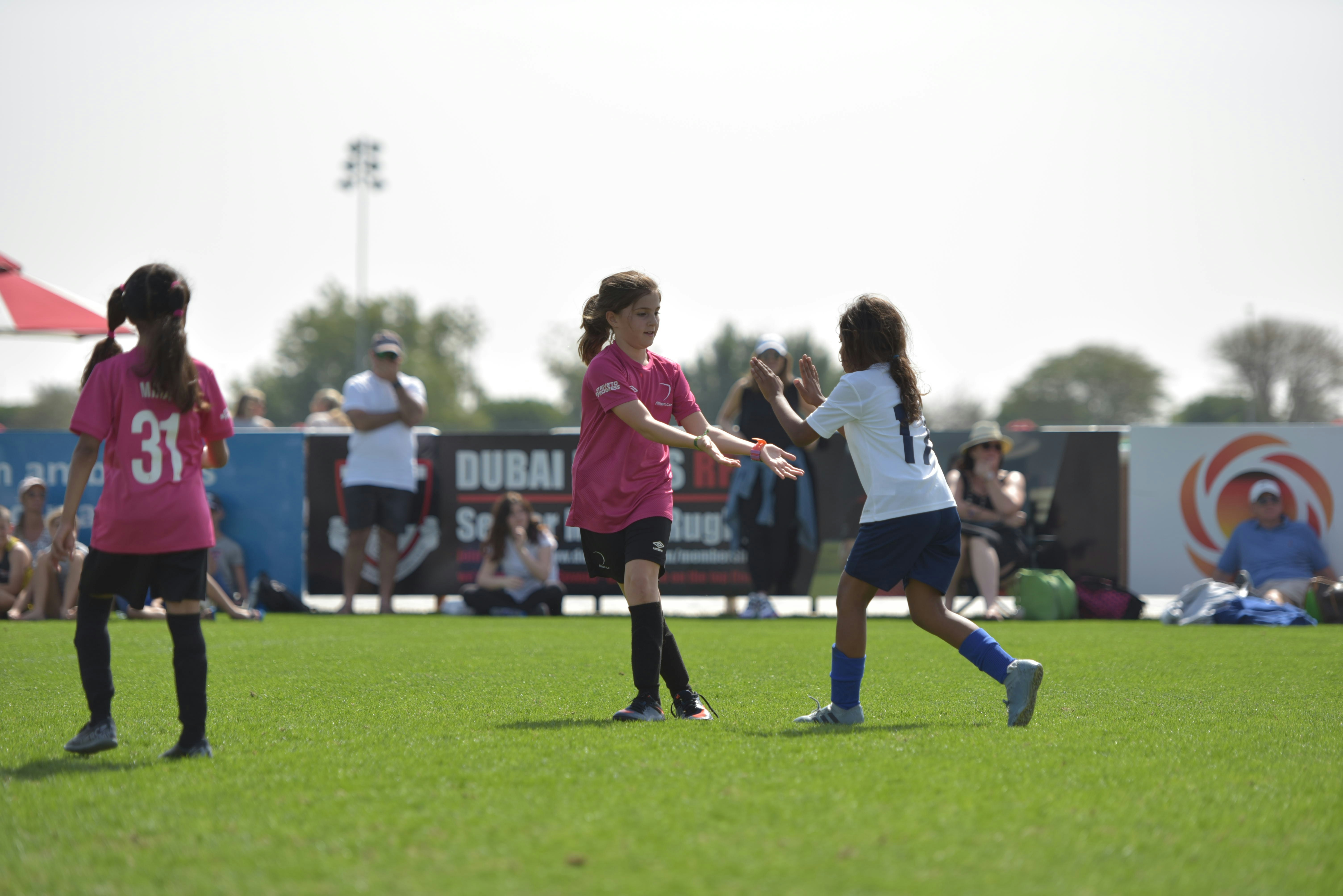 Young girls playing soccer on green field during Dubai sports tournament