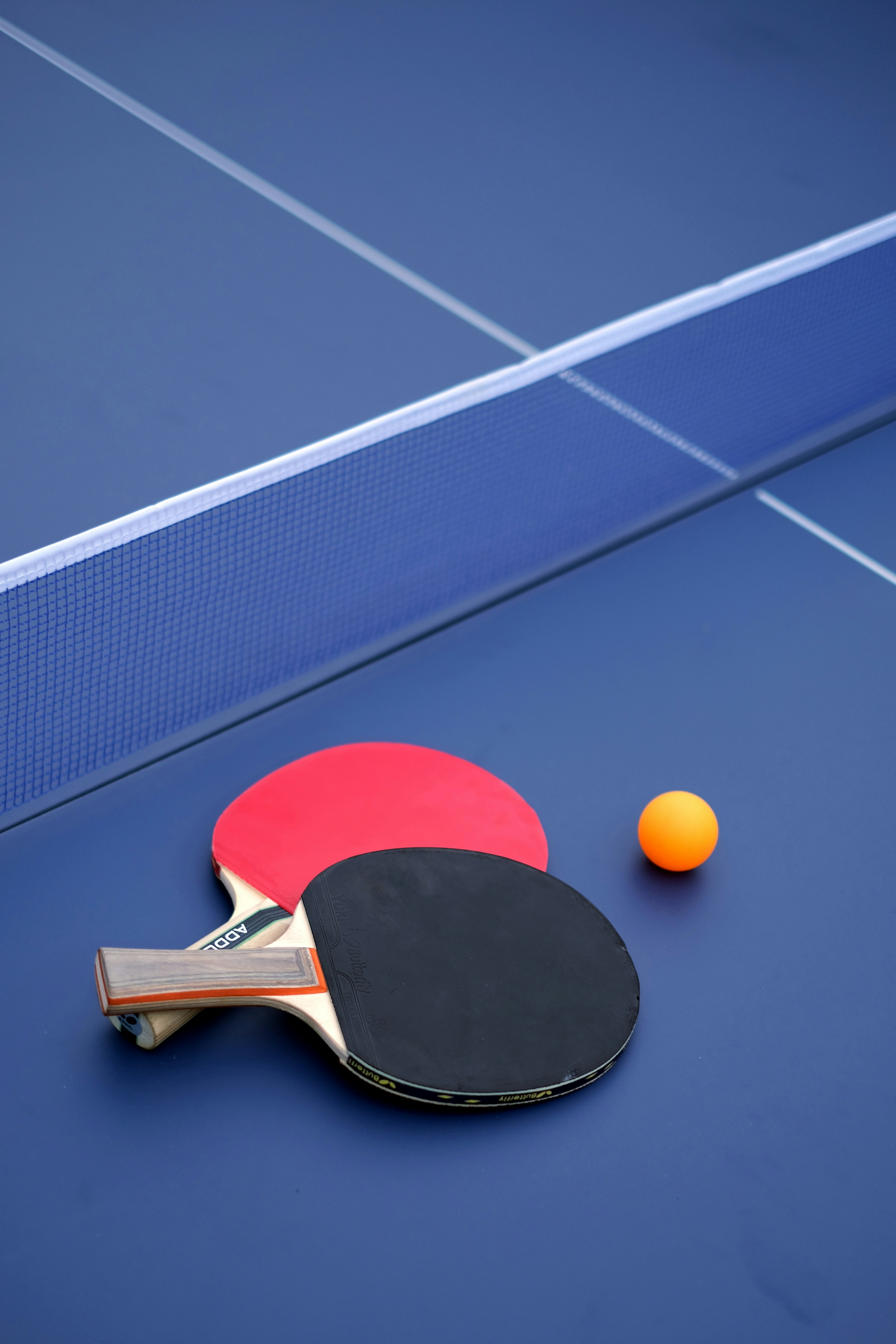 Red and black table tennis paddles with orange ball on blue ping pong table