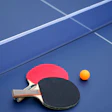 Red and black table tennis paddles with orange ball on blue ping pong table