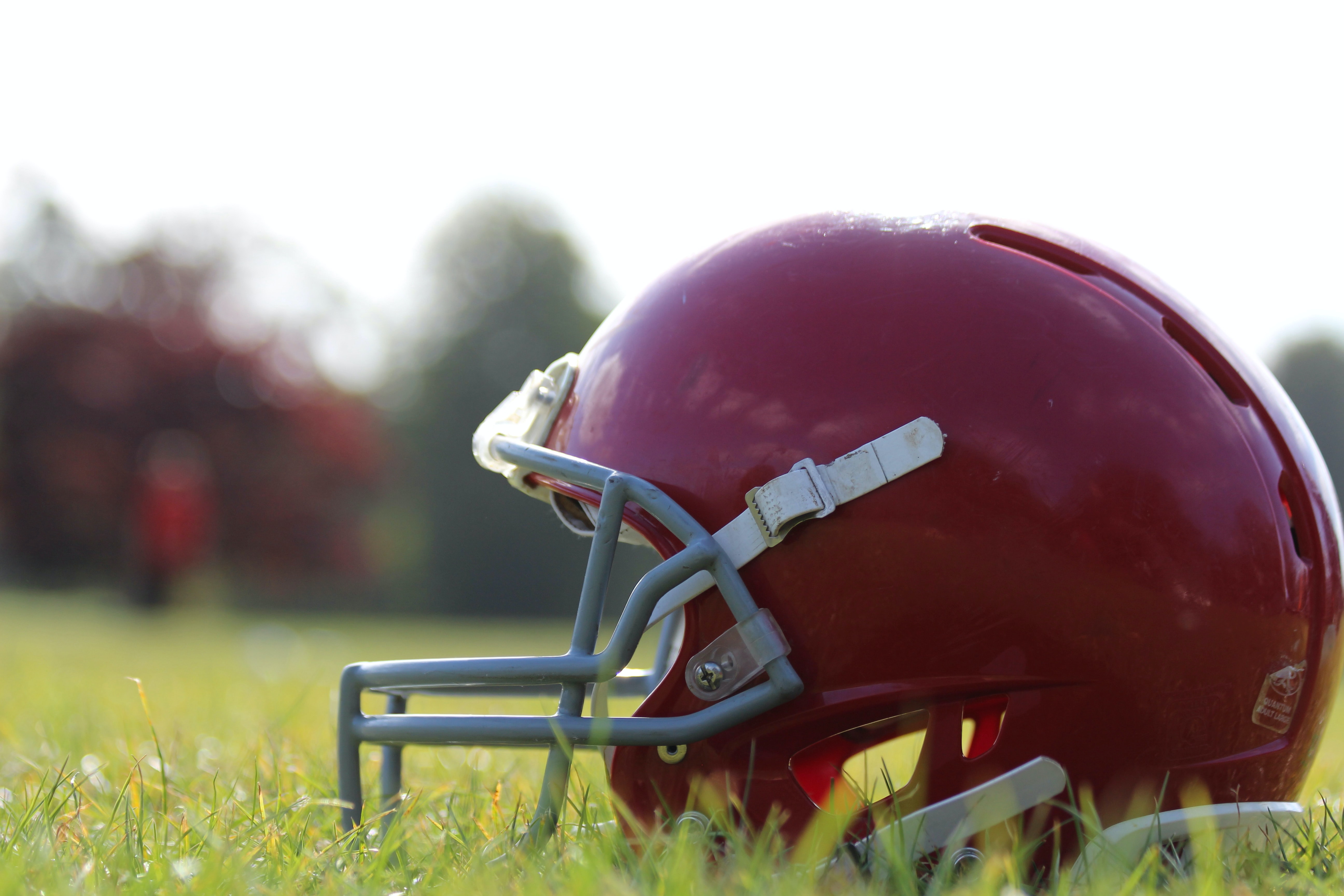 Red football helmet resting on grassy field with blurred background