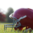 Red football helmet resting on grassy field with blurred background