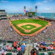 Packed baseball stadium with ocean view, green field, and large video scoreboard