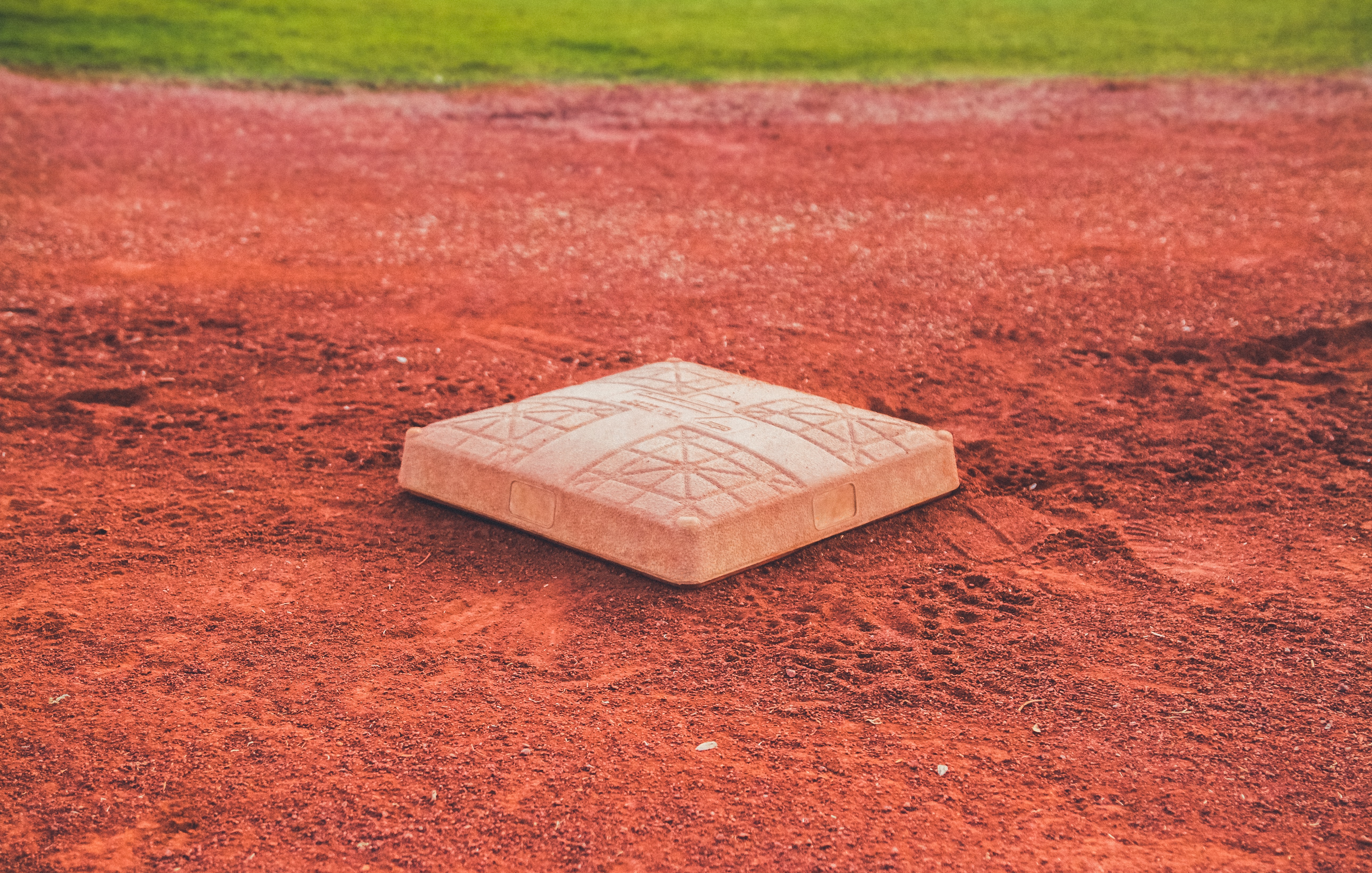 White baseball base on red clay baseball field with green grass background