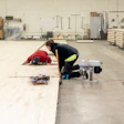 Two workers installing flooring in an industrial warehouse workshop