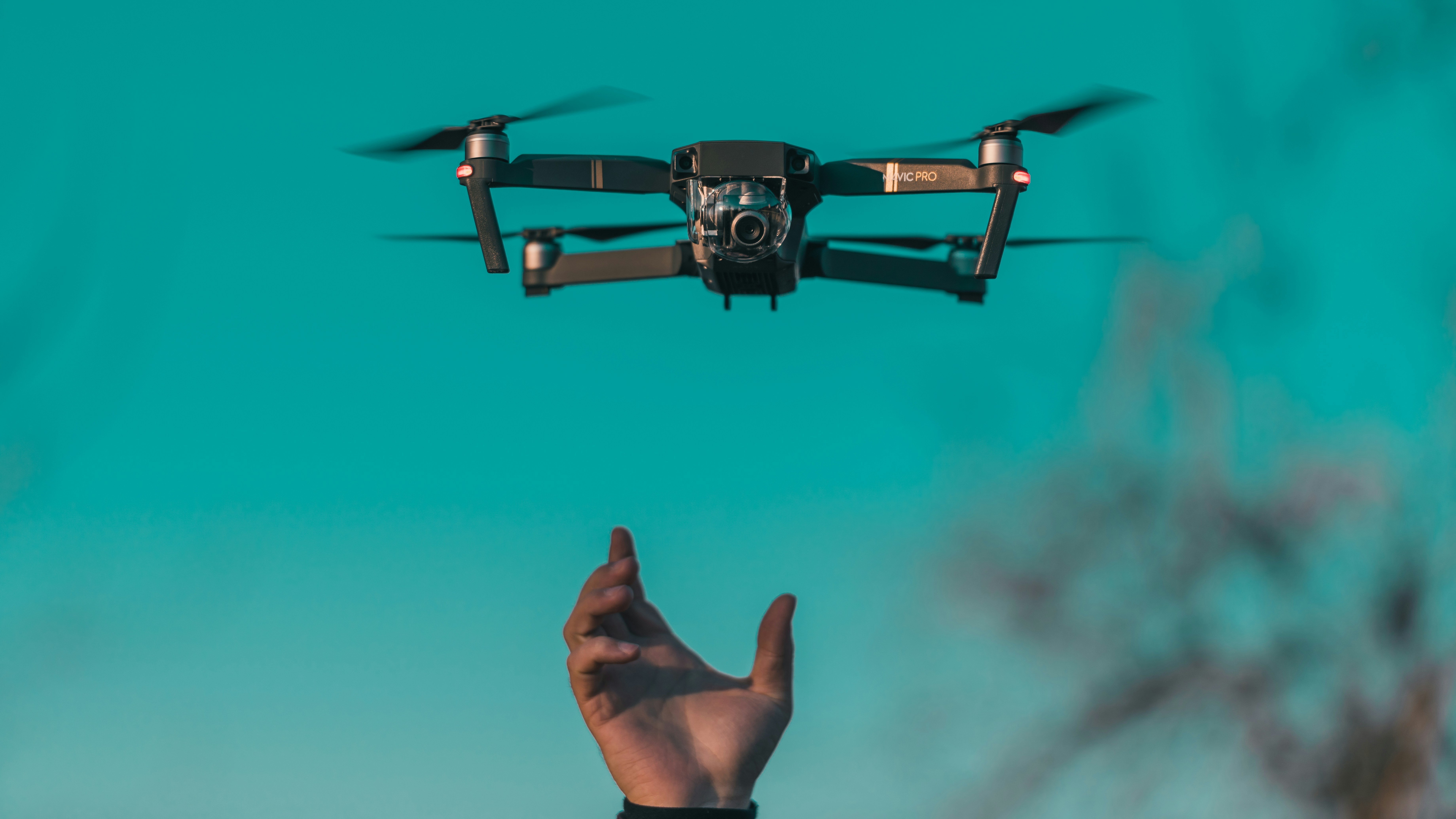 Drone hovering mid-air against teal background with outstretched hand below