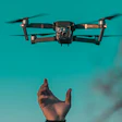 Drone hovering mid-air against teal background with outstretched hand below