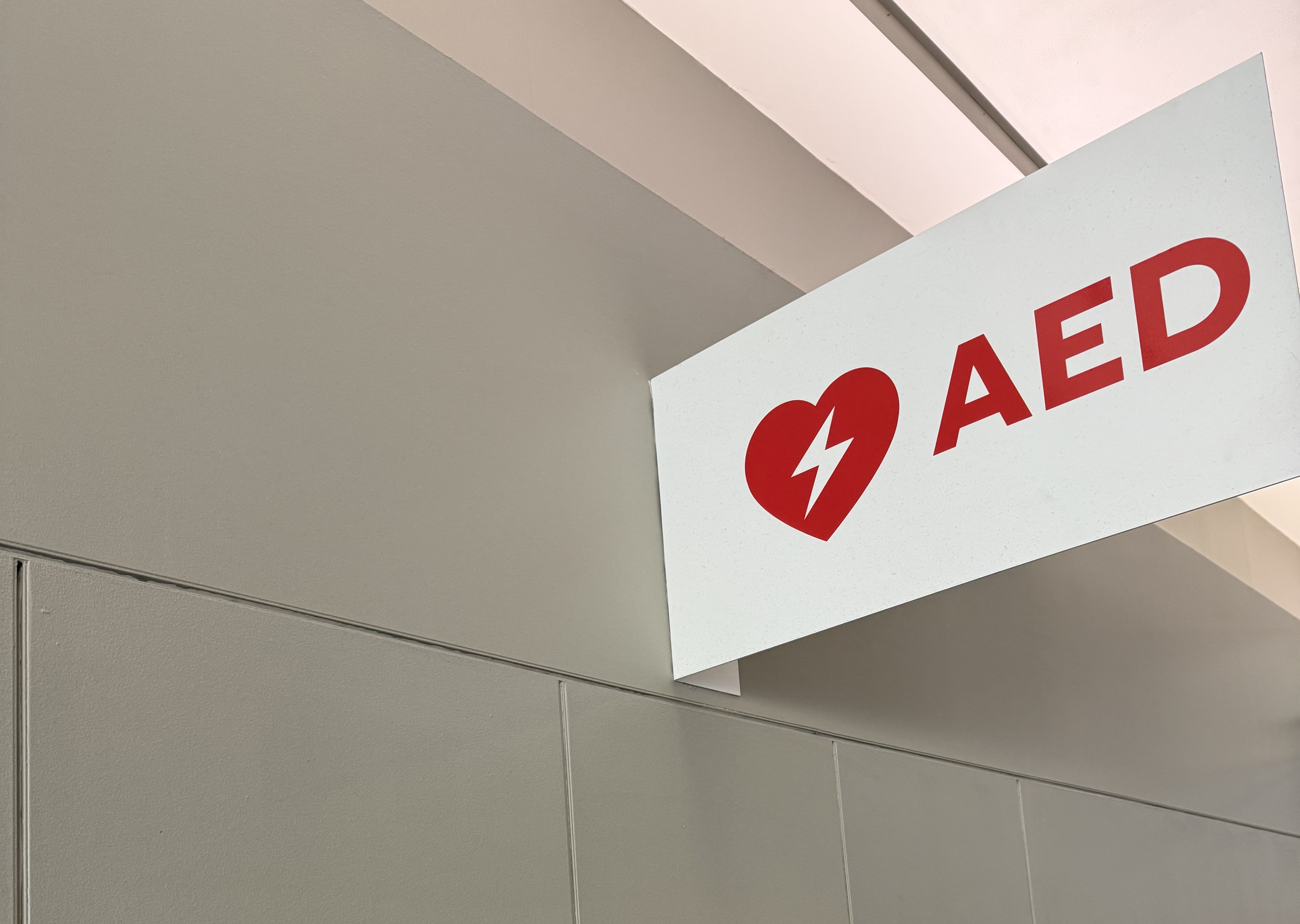 Red AED emergency sign mounted on white wall indicating defibrillator location