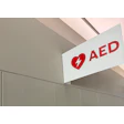 Red AED emergency sign mounted on white wall indicating defibrillator location