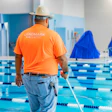 Pool maintenance worker in orange shirt cleaning swimming pool lanes
