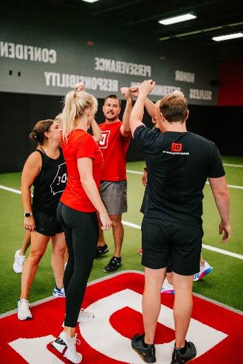 Fitness team high-fiving in red and black athletic wear on indoor training floor