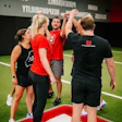 Fitness team high-fiving in red and black athletic wear on indoor training floor