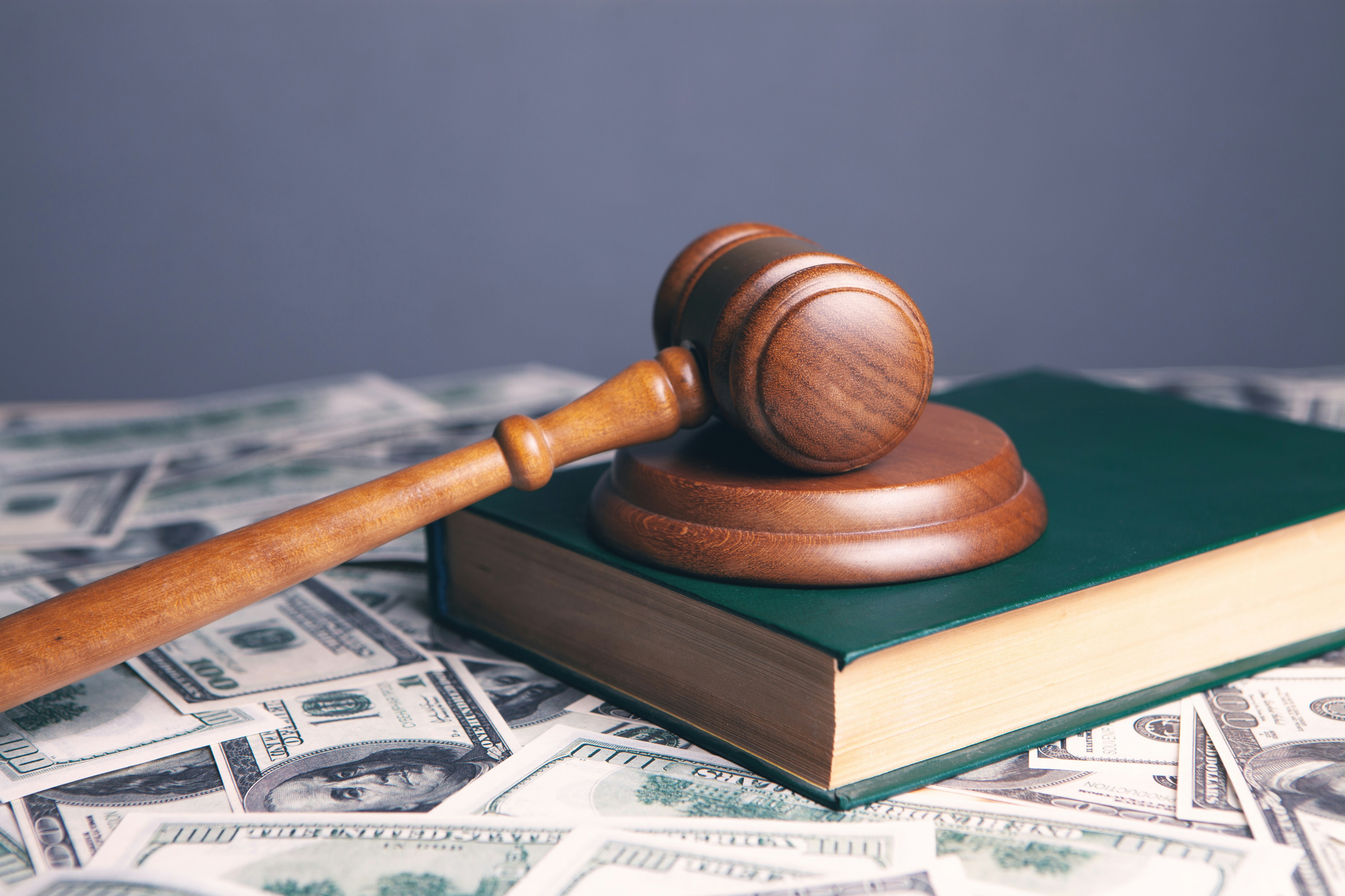 Wooden judge's gavel resting on green book with scattered US dollar bills