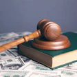 Wooden judge's gavel resting on green book with scattered US dollar bills