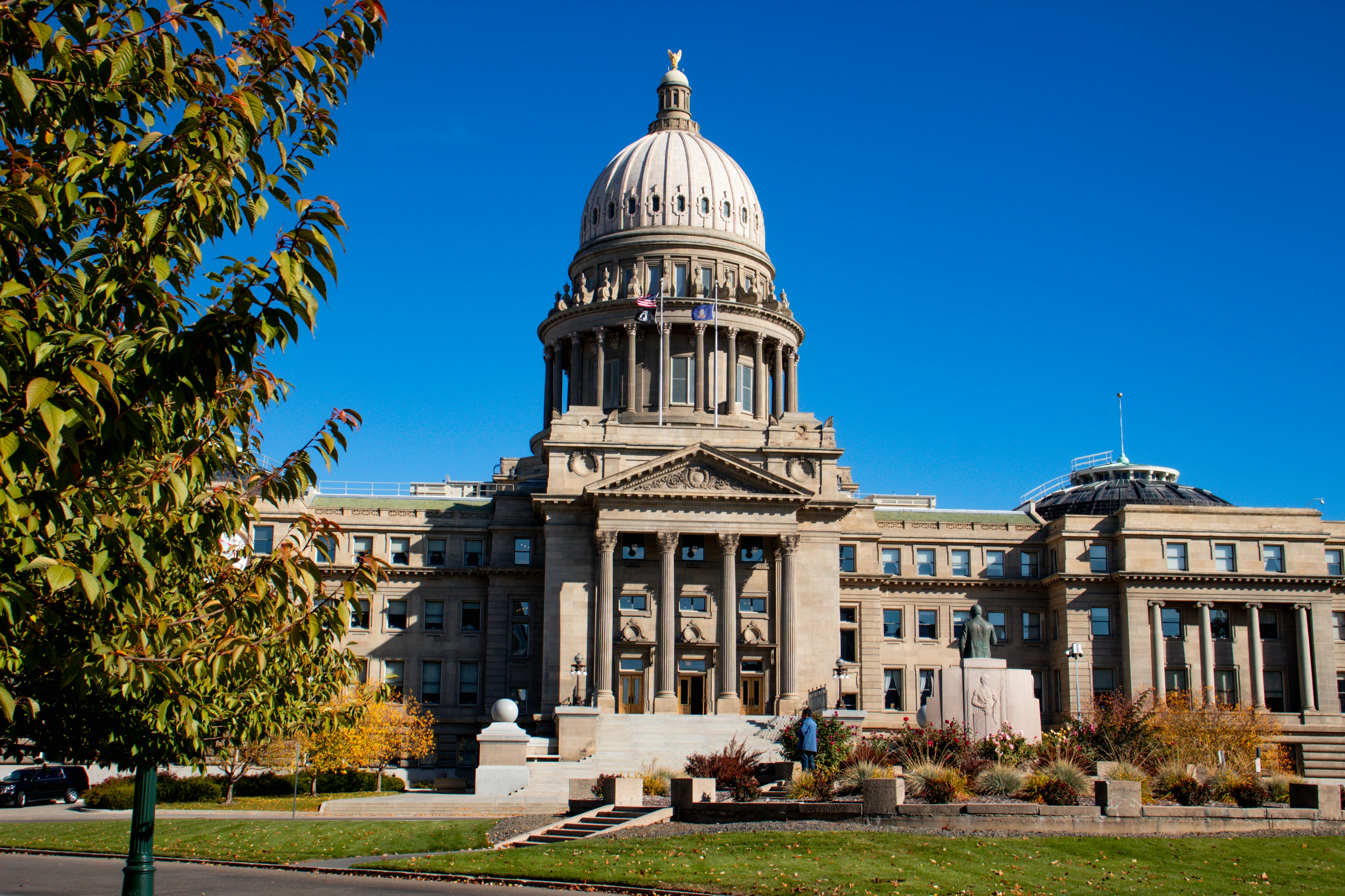 Idaho State Capitol building with white dome, columns, and autumn trees under blue sky