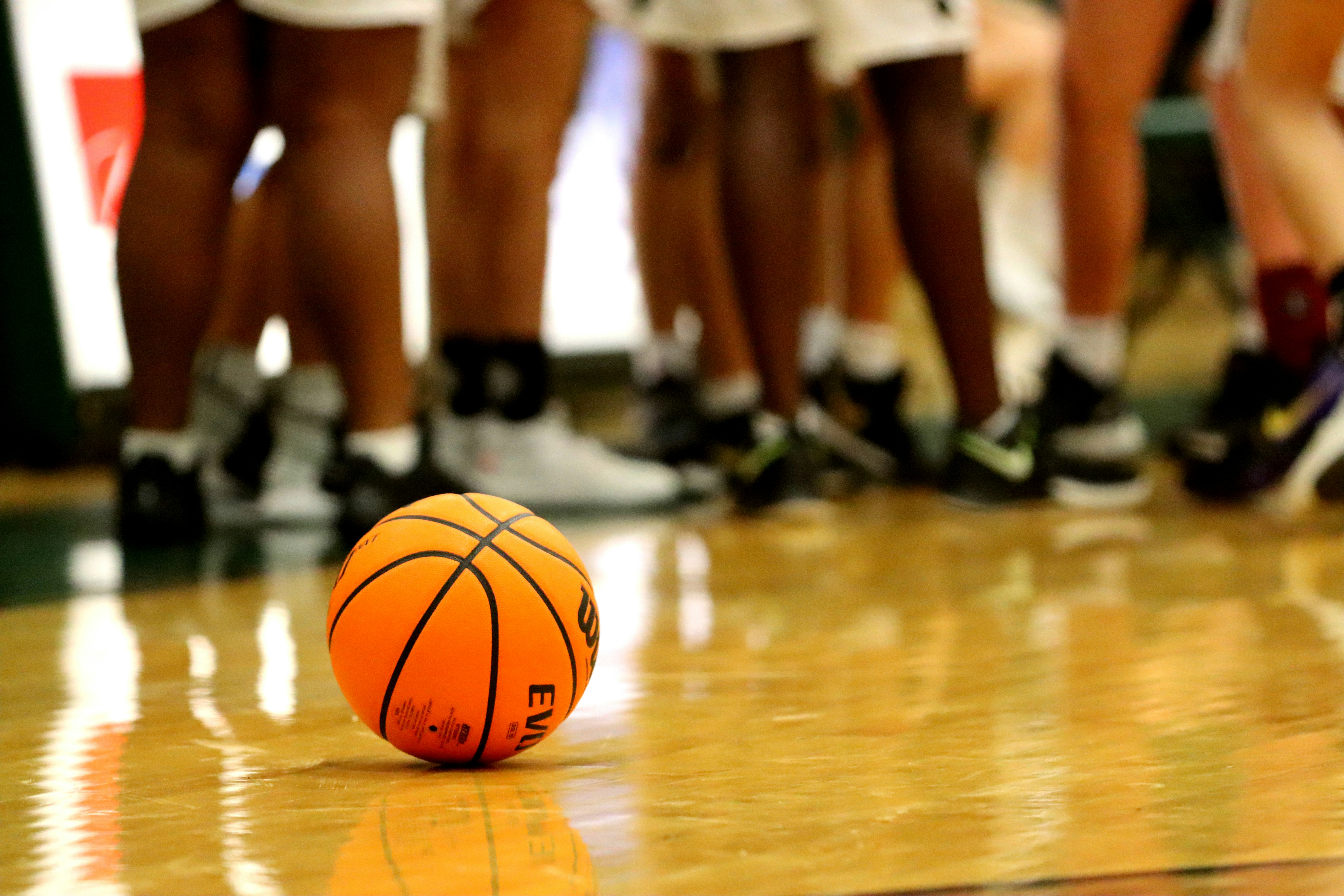 Orange Spalding basketball resting on a hardwood court surrounded by players' legs during a basketball game