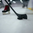 Hockey stick blade touching black puck on ice rink surface
