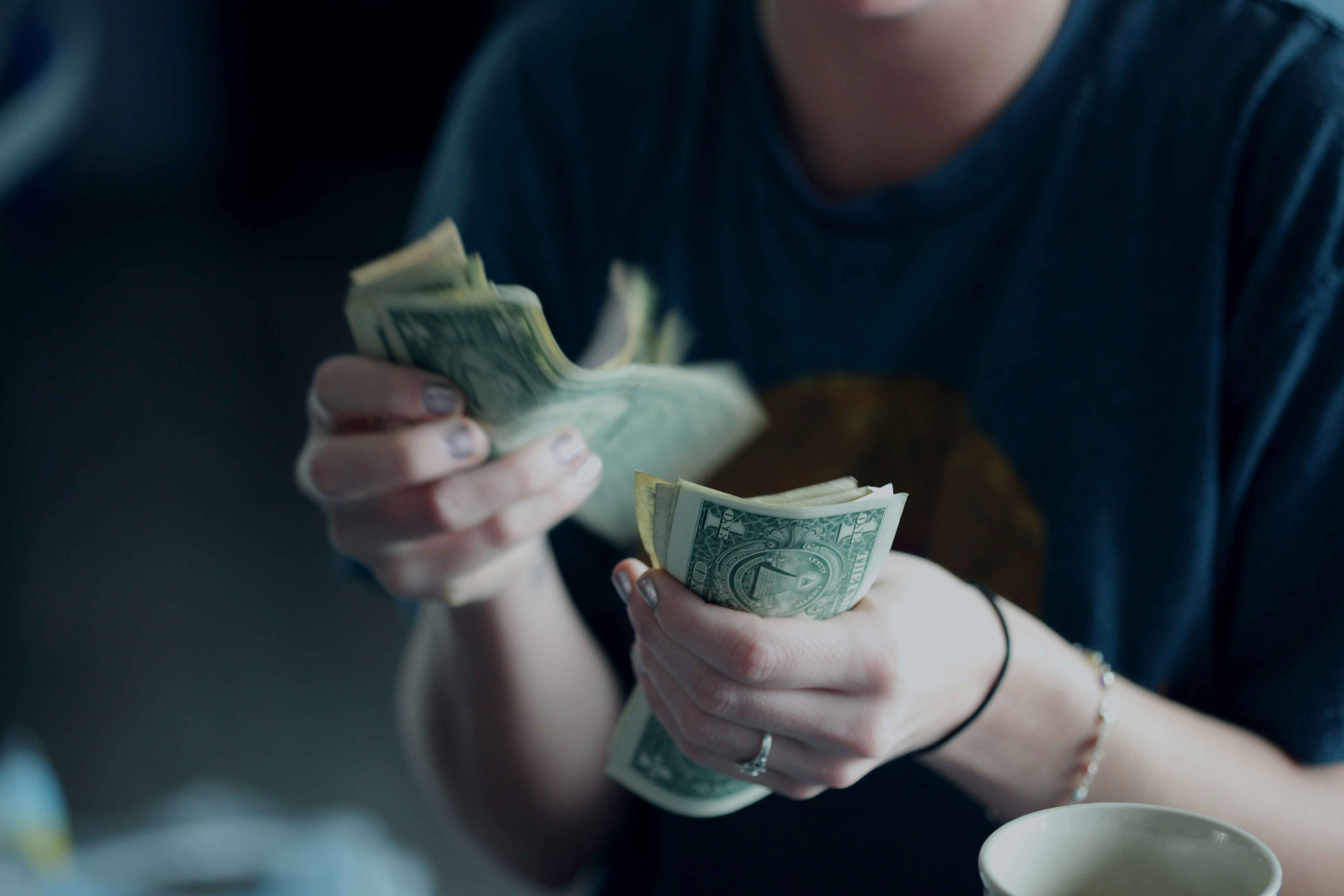 Person in dark shirt counting US dollar bills in hands