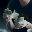 Person in dark shirt counting US dollar bills in hands