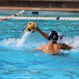 Water polo player in black cap with number 9 throws yellow ball during competitive match in pool