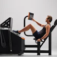 Man using leg press exercise machine while checking digital fitness device