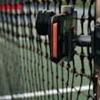 Close-up of a black and red gate latch mechanism mounted on a green metal fence